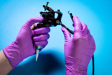 Hands In Pink Rubber Gloves Hold A Tattoo Machine On A Blue Backgroundの写真素材