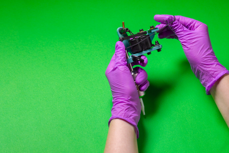 Hands In Pink Rubber Gloves Hold A Blue Tattoo Machine On A Green Backgroundの写真素材