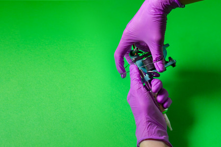 Hands In Pink Rubber Gloves Hold A Blue Tattoo Machine On A Green Backgroundの写真素材