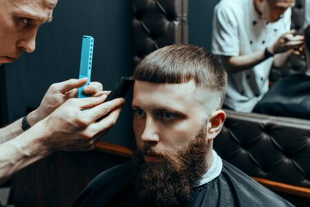 BARBERSHOP THEME. BARBER IS TRIMMING THE HAIRCUT OF HIS YOUNG SERIOUS CLIENT. HE IS USING A HAIR...