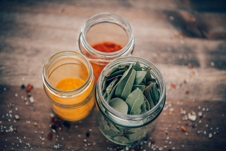 Bay leaves, turmeric and paprika powder in jars on a wooden table.の写真素材