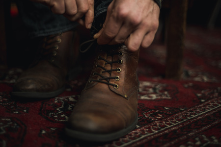 Closeup of male hands lacing up and tying his old brown leather boots.の写真素材