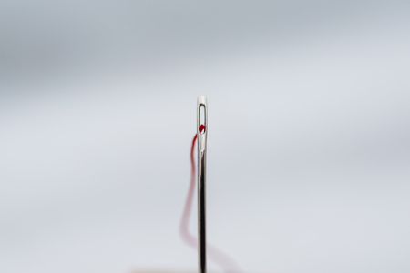 Close up of a silver needle and a red wool thread.