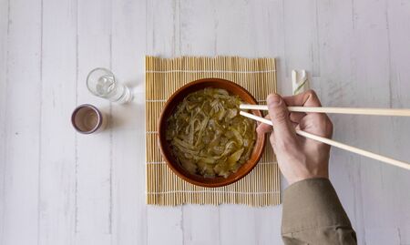 eating a japanese soup with chopsticks on a bamboo mat with white wooden background