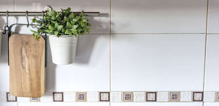 white kitchen wall with border in brown tones with hanging plant and wooden boardの写真素材