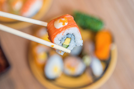Sushi roll : Roll sushi held by chopsticks from background of assorted sushi setの写真素材