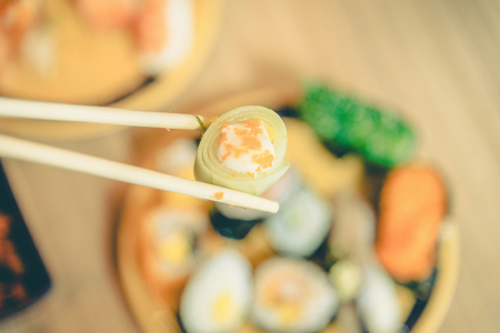 Sushi roll : Roll sushi held by chopsticks from background of assorted sushi set ,vintageの写真素材