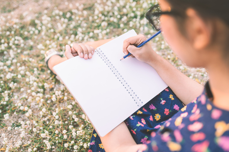 woman writing in her diary on the meadow with white flowersの写真素材