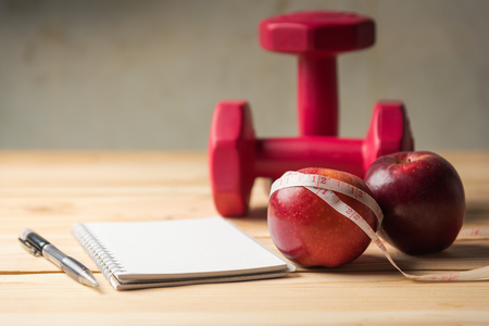 apple and measuring tape and Pair of red 1 kg dumbbells on woodenの写真素材