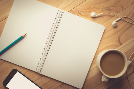 Relax workplace - Top view of Smartphone with blank screen, earphones, notebook and coffee on wooden background , vintage toneの写真素材