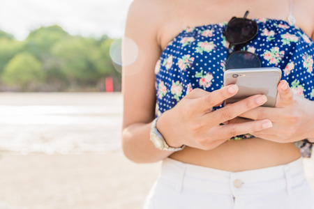 Beautiful woman's hand using smart phone at beachの写真素材