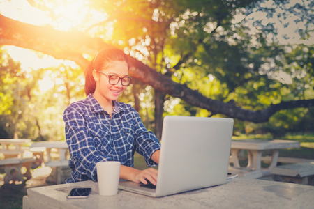 Beautiful hipster asian woman using laptop in park on sunset. Vintage tone. asian business woman using laptop.の写真素材