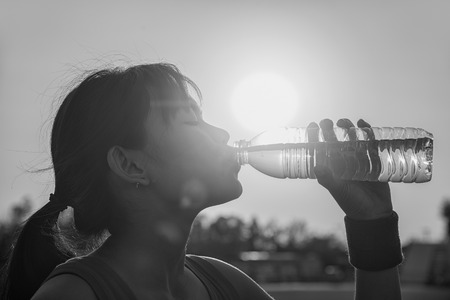 Female drinking a bottle of water  , sunset ,  black and whiteの写真素材