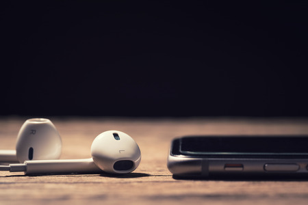 Headphone and phone media portable on dark tone. headphone and smartphone on wood table. headphones and phone depth of field. White headphone and black smartphone. selective focus of headphone.の写真素材
