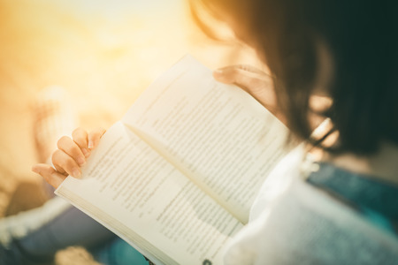 A young woman reading a book. Book in woman hands , sunset  vintage toneの写真素材