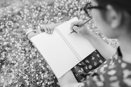 woman writing in her diary on the meadow with white flowers , black and whiteの写真素材