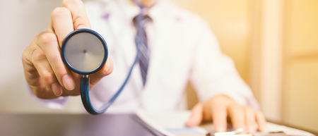 A doctor holds his stethoscope to insinuate that it's time for a check up in clinic banner panoramic crop for copy space.の写真素材