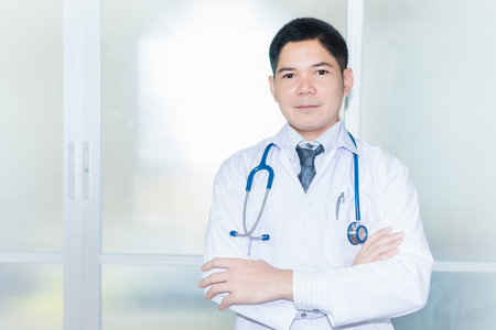 Smiling doctor posing with arms crossed in the office, he is wearing a stethoscopeの写真素材