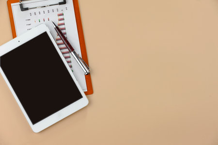 Tablet computer and stationery on beige background, top view. Space for text