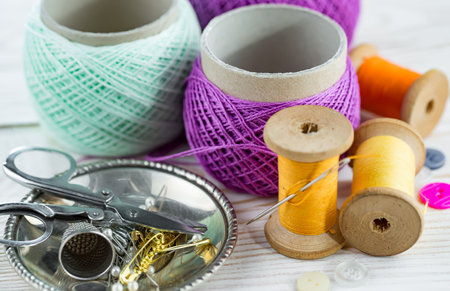Spools of thread, scissors, thimble and pins on white wooden background