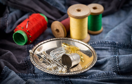 Spools of thread, thimble and buttons on jeans background.