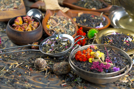 Dry tea leaves and flowers in metal bowls on old wooden tableの写真素材