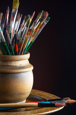 Paint brushes and paints in a clay pot on a black backgroundの写真素材