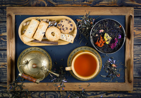 Dry tea leaves in a cup, teapot and cookies on wooden backgroundの写真素材