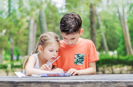 Hapy kids  learn in a park. Brother and sister together do the job. Boy and girl sitting at the table and doing exercise.の写真素材