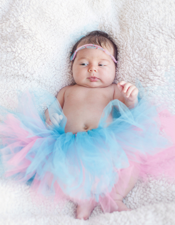 Portrait of a newborn girl with a pink-and-blue skirt and hair decoration rim on the head. Gentle photo with natural light.の写真素材