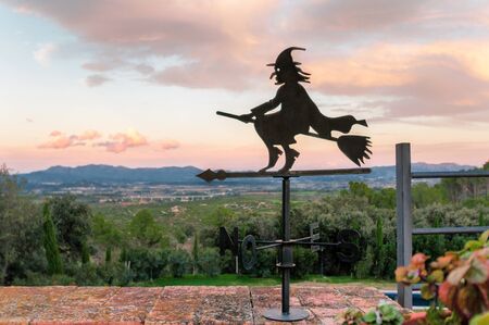 Weathervane and wind signs in the form of a witch on a broomstick with a sunset sky.の写真素材
