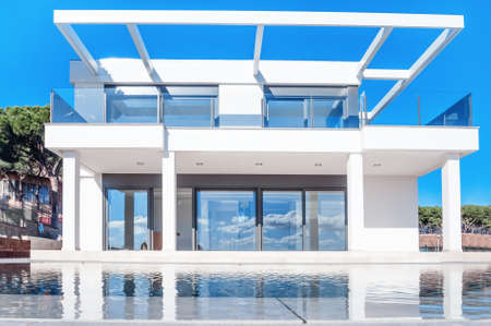 Luxury modern white house with large windows overlooking a Mediterian landscaped garden with palm trees and  blue swimming pool. High tech style house.のeditorial素材