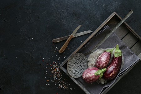 Eggplant varieties in black bowl over dark slate background. Overhead view.