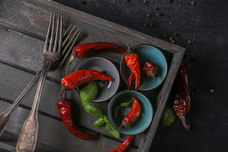 chili peppers with basil and peppercorns in bowls on a rustic surface,