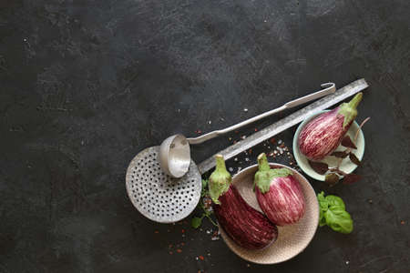 Eggplant varieties in black bowl over dark slate background. Overhead view.