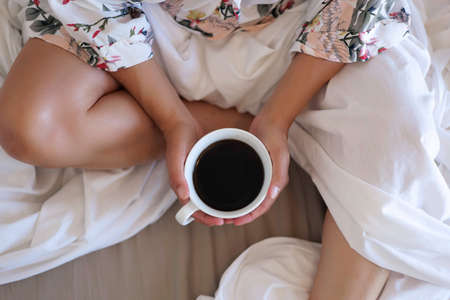 close up of young woman with cup of coffee in bed at homeの写真素材