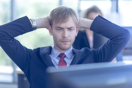 A young white businessman Wearing a red tie and suit sitting in front of a computer screen with a...