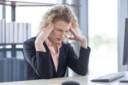 A businesswoman with curly blonde hair resting her hands on her head, feeling anxious, serious and...