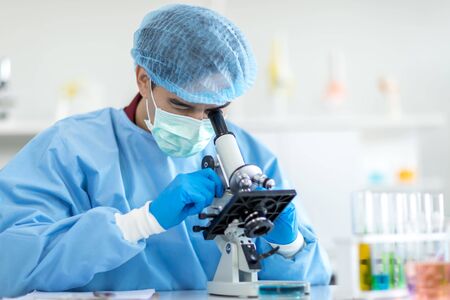 Asian scientists wear protective clothing looking for microscopes while doing medical research in a...