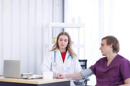 A female doctor wearing a white coat with a stethoscope is checking the blood pressure of the...