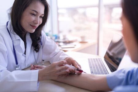 Asian female doctor wearing a white coat is injecting the arm of a female patient. Medicine and health care, female doctors and female patients concept.の写真素材