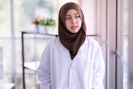 Portrait of smiling Muslim female doctor and standing looking at the hospital window.の写真素材