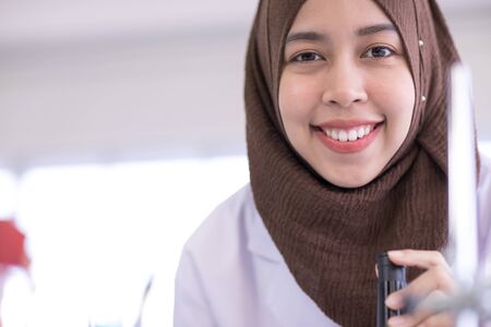 A female muslim scientist in white gown with microscope and smiling to camera in laboratoryの写真素材