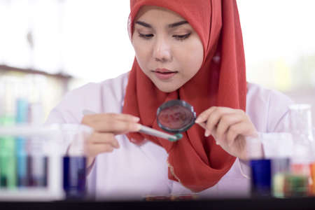 Muslim woman's dress in white. Look at the magnifying glass during a chemistry lab experiment.の写真素材
