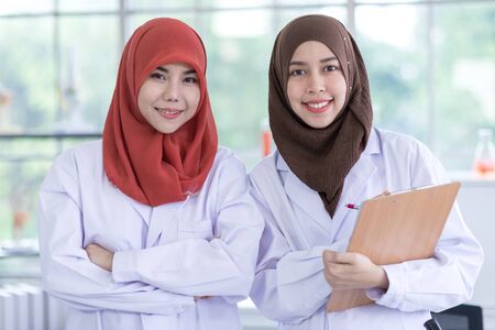 Two Muslim female scientists wearing white gown. Both smiled at to camera in a chemistry lab.の写真素材