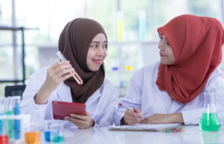 Two female muslim scientists wear white coat  with reagent during experiment in chemical lab.