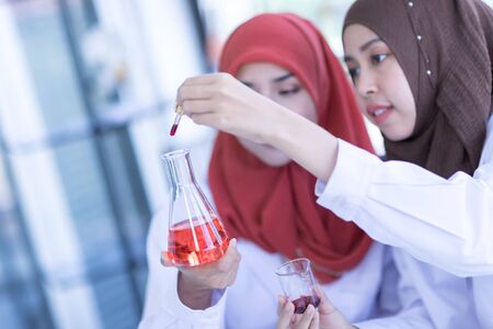 Two female Muslim scientists wear a white coat and look at a glass test tube during an experiment in a chemical laboratory.の写真素材
