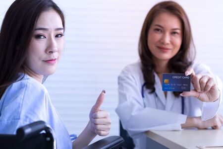 Female doctor holding a credit card and an Asian woman looking at the cameraの写真素材