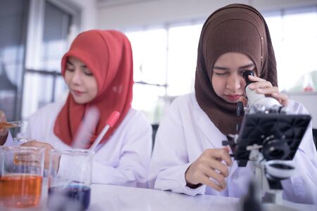 Beautiful female muslim scientist looking through microscope during experiment in chemical laboratoryの写真素材