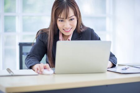 Beautiful Asian business woman wore a black suit sitting in the office, smiling happily when the job...
